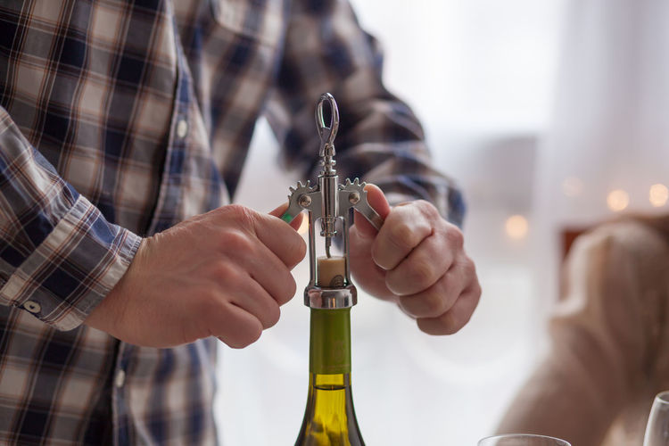 Close up of unrecognizable man opening wine bottle with corkscrew.