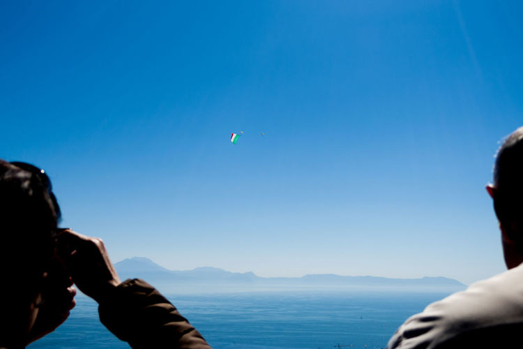 People flying over sea against clear blue sky