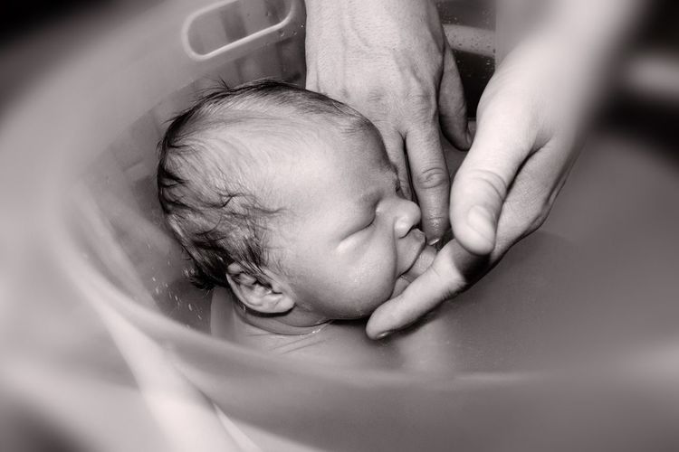 Cropped image of woman bathing baby in tub