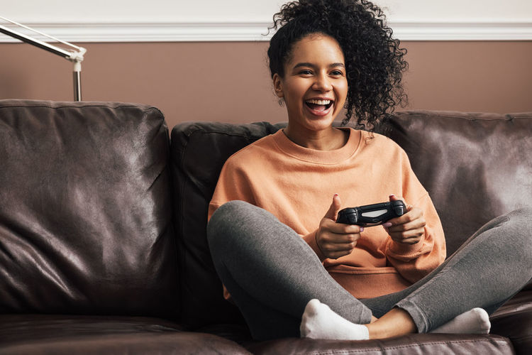 Smiling young woman playing video game sitting on sofa