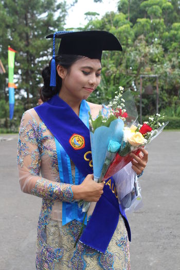 Young woman holding bouquet during graduation in college