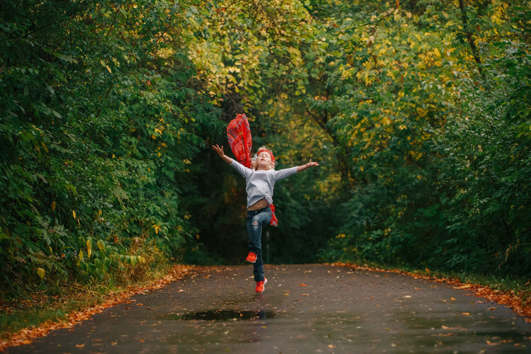 Cute girl jumping on road in forest during autumn