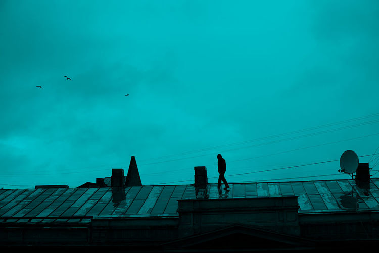 Low angle view of silhouette of man on rooftop against sky