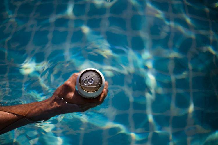 Selective focus white beer can in hand. man is soaking in the pool 