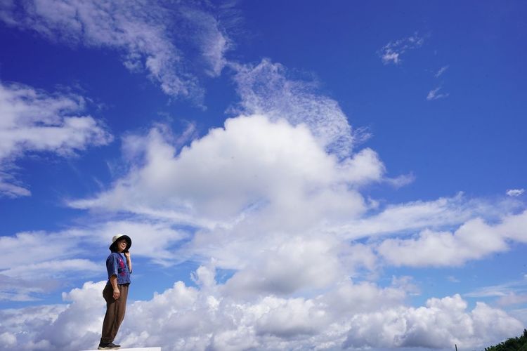 Low angle view of boy standing against blue sky