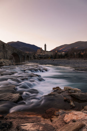 Landscape of a medieval bridge over a turbulent river at sunset in winter