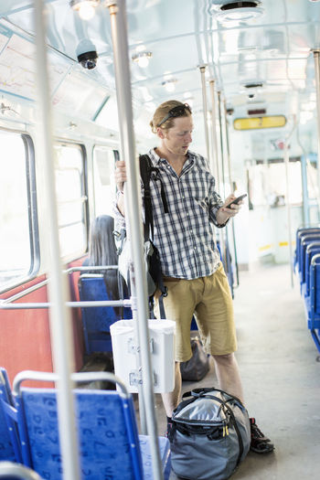 Man using mobile phone while standing by luggage in metro train