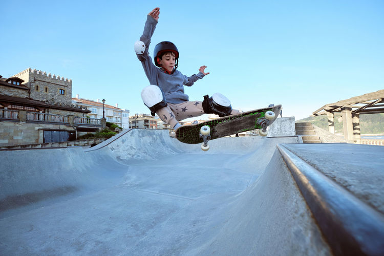 Teen boy in protective helmet riding skateboard in skate park on sunny day on seashore