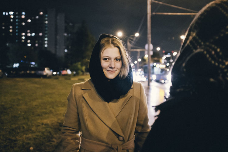 Portrait of smiling young woman standing in city at night