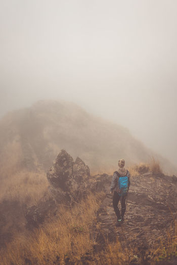 Rear view of backpack woman standing on cliff during foggy weather