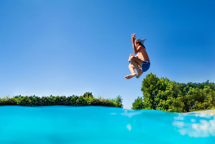 Low angle view of woman jumping on beach against blue sky