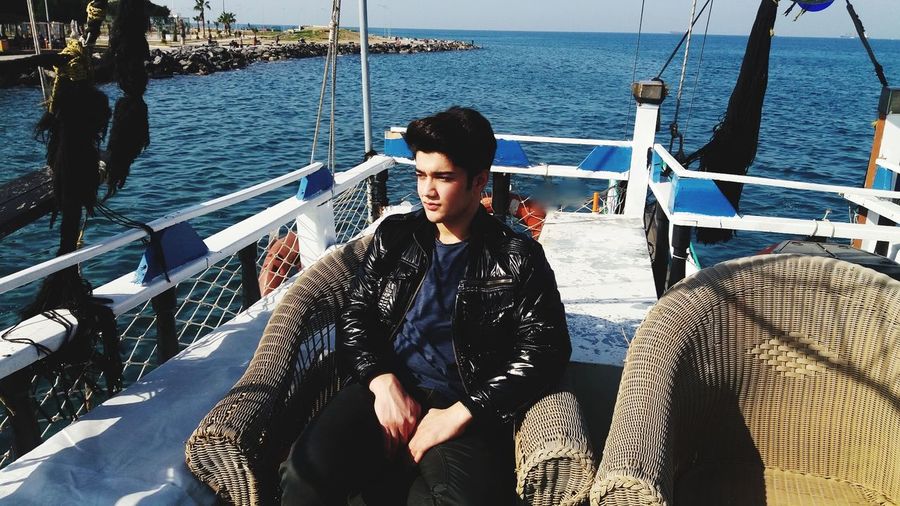 Handsome young man sitting on chair in boat at sea