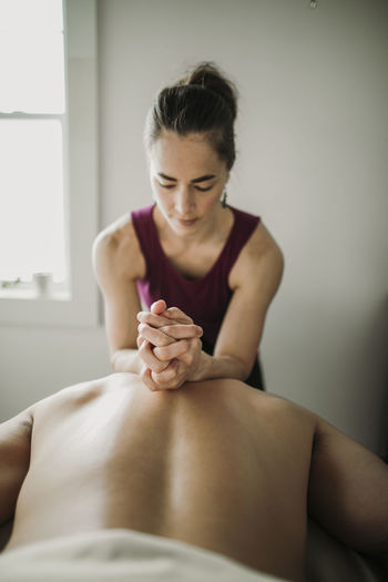 Female massage therapist uses forearms to work on male patient's back