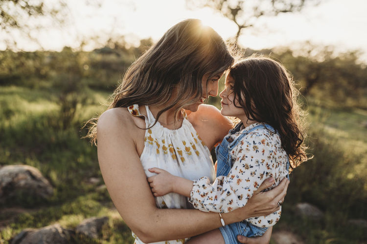 Young mother holding daughter and cuddling in bright california field