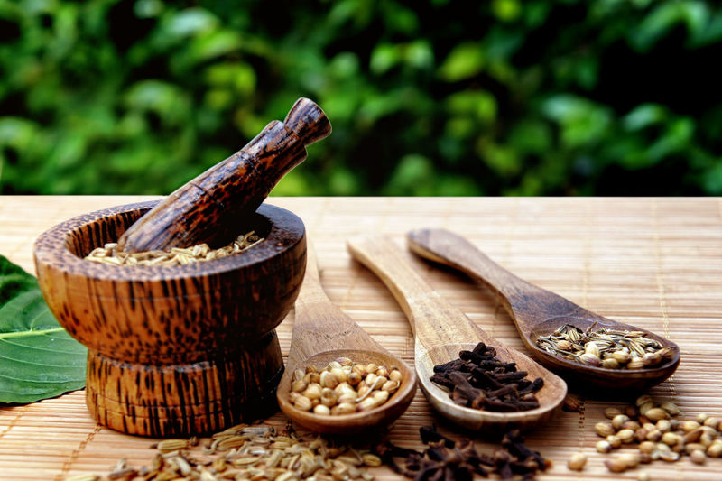 Close-up of spices and herbs with mortar and pestle by wooden spoons on table