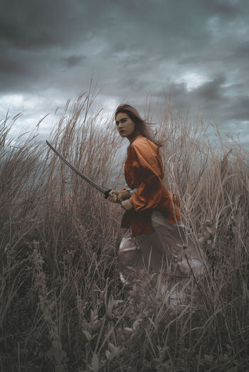 Young woman standing on field against sky