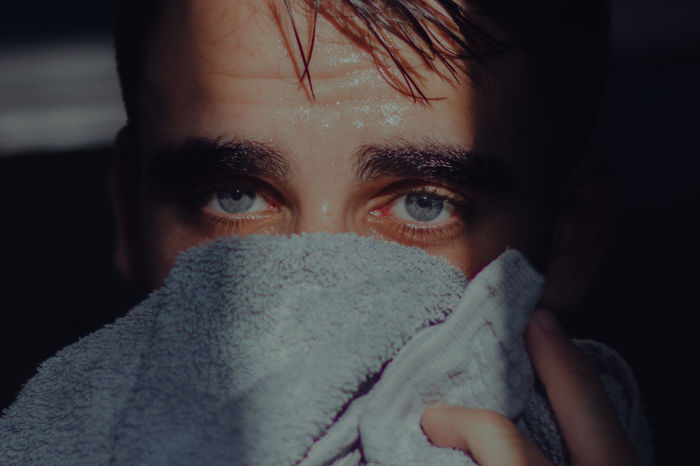 Close-up portrait of young man covering face with towel at home