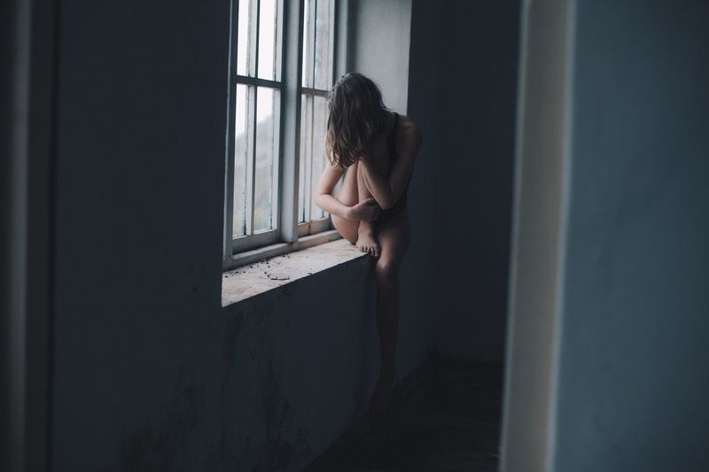 Woman sitting on window sill in abandoned building