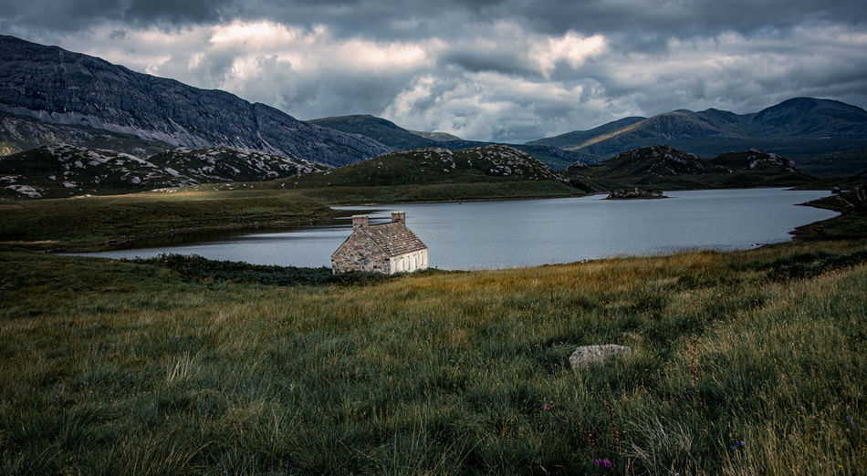 A remote highland bothy sitting on the banks of loch stack.with mountain tops of arkle in background