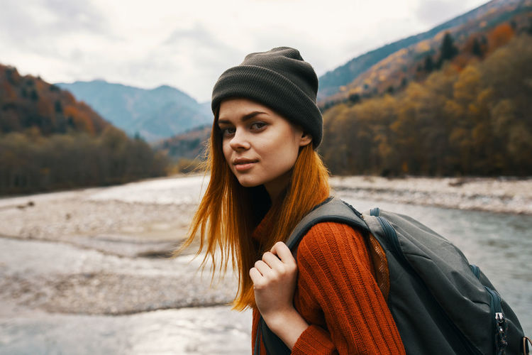 Portrait of beautiful young woman standing by mountains