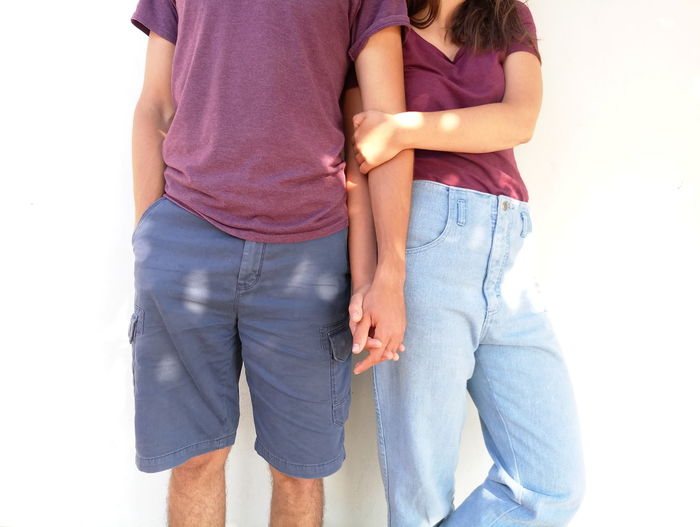 Midsection of couple holding hands against white wall