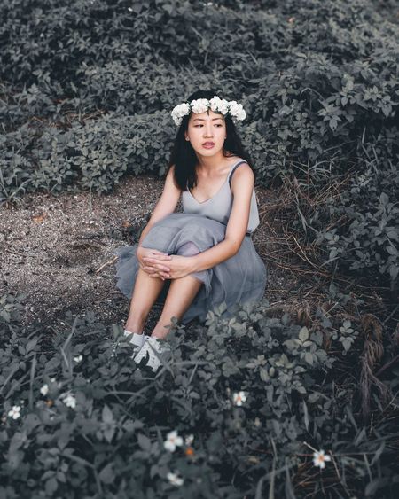 Thoughtful woman wearing flowers sitting on field amidst plants