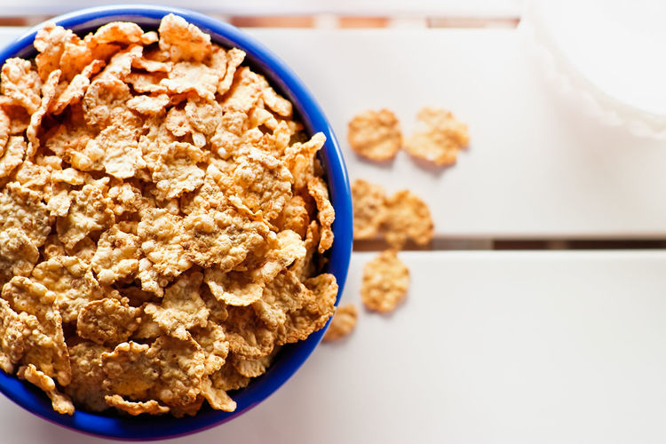 Cornflakes in a blue bowl on white wooden table