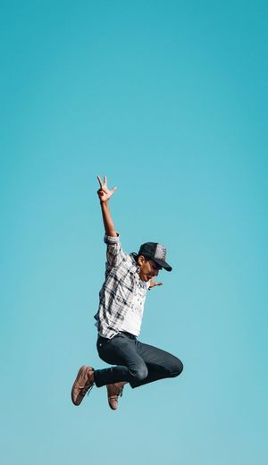 Low angle view of person jumping against clear blue sky