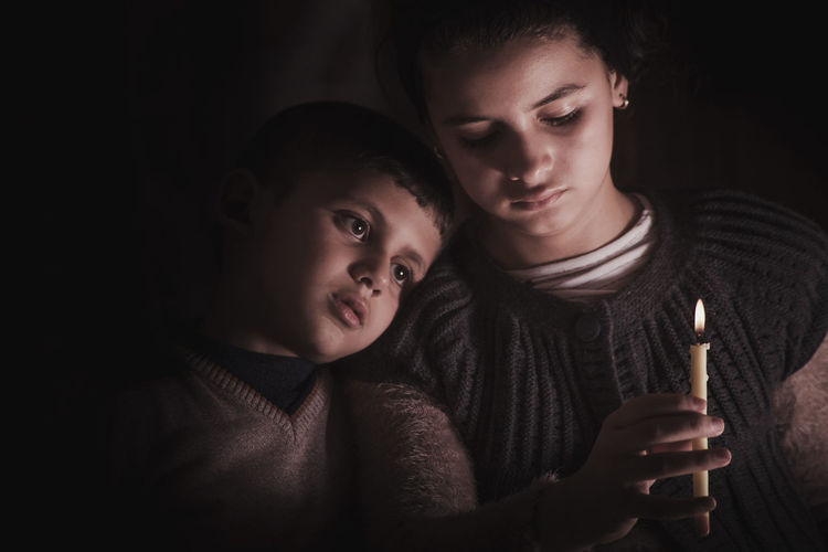 Close-up of sad siblings holding candle in darkroom