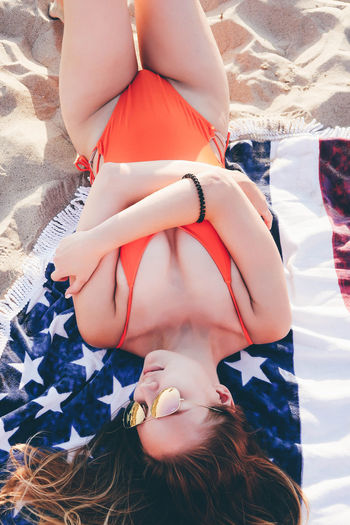 High angle view of young woman wearing sunglasses while lying on blanket at beach