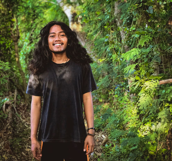 Portrait of young man smiling while standing in forest