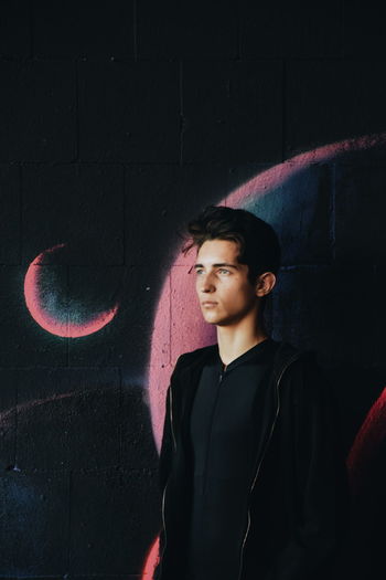 Young man standing against wall with graffiti