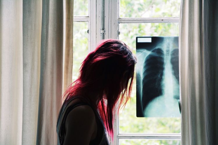 Side view of woman with dyed hair standing by x-ray on window at home