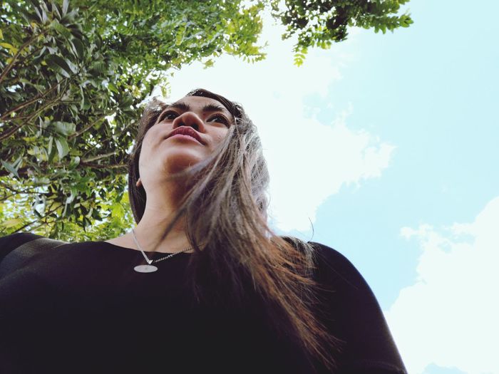 Low angle view of woman looking at tree against sky
