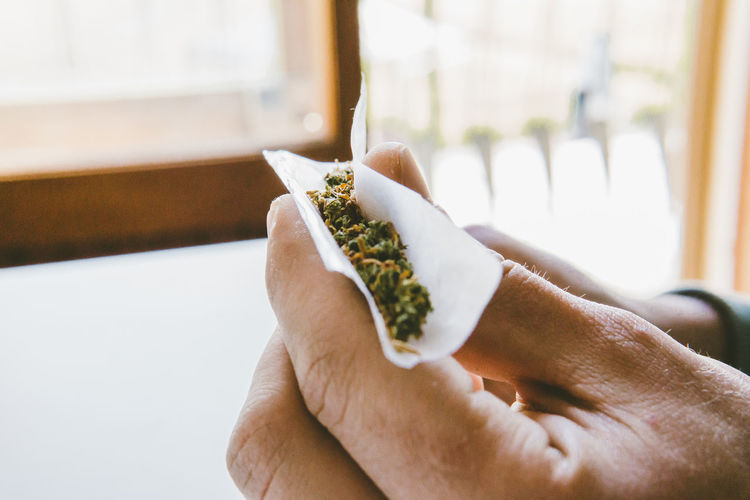 Cropped hand of man rolling marijuana joints in paper at home