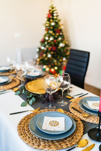 Festive table setting near decorated christmas tree with glowing garlands before christmas celebration party