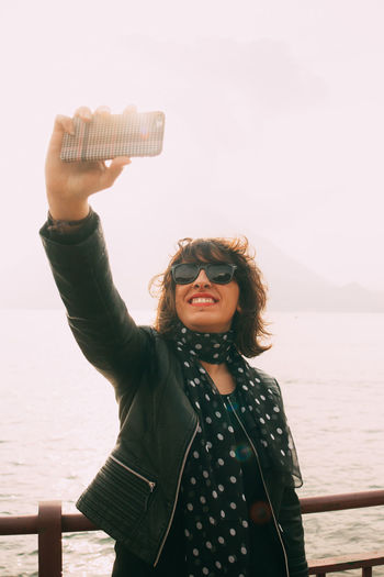 Smiling woman taking selfie by sea against clear sky