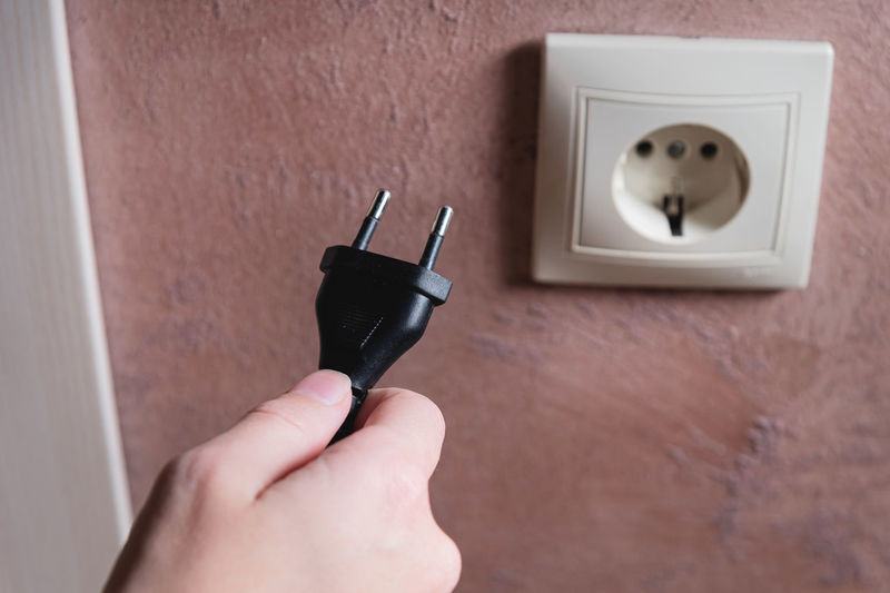 A woman's hand inserts an electric plug into a socket, close-up