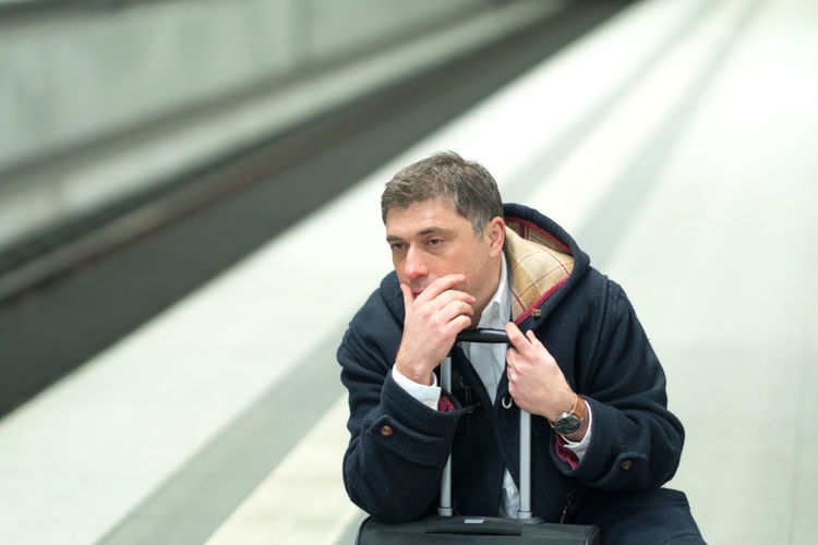 Man with hands covering mouth sitting at railroad station platform