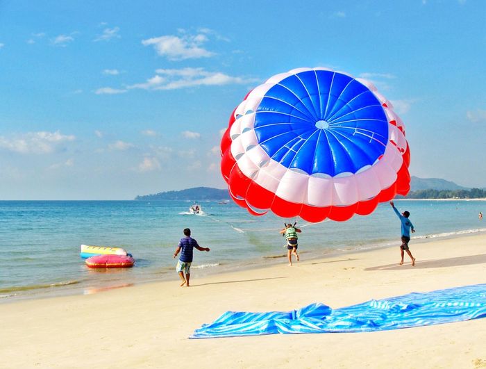 Rear view of people enjoying paragliding at beach against sky