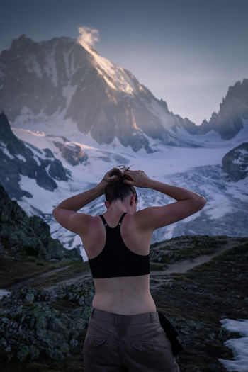 Rear view of woman tying hair while standing against mountain during winter