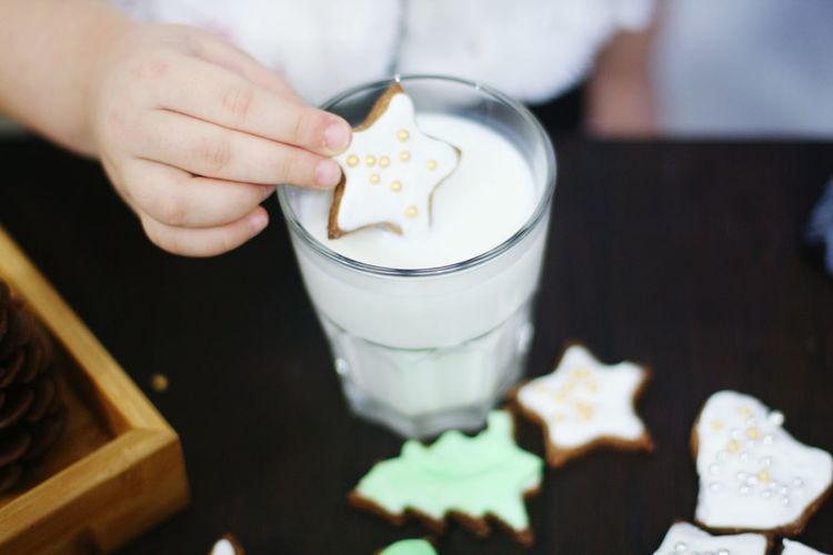 Cropped image of child dunking star shape cookie in milk