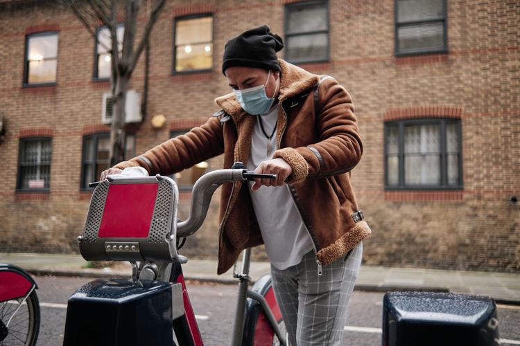 Young man wearing a face mask grabbing a bicycle on the street