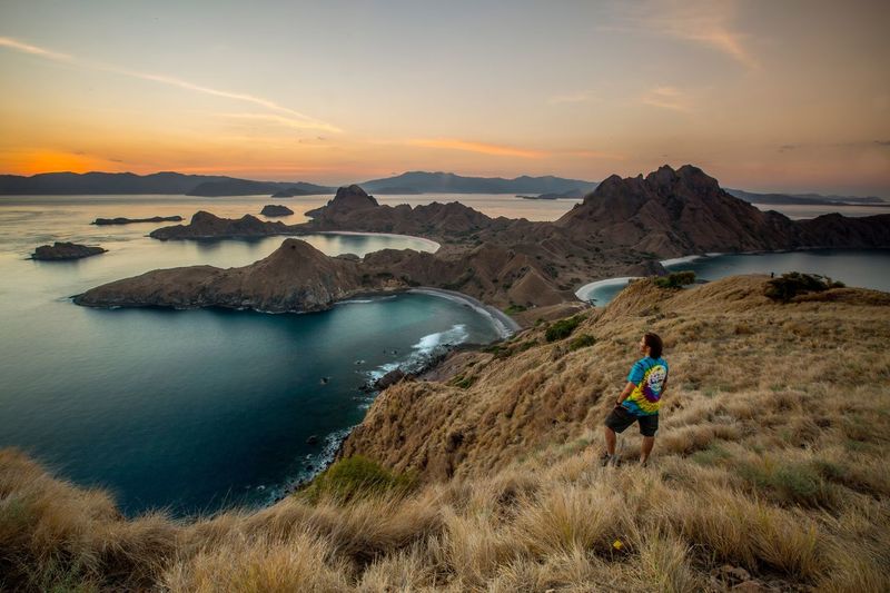 A man alone facing the sunset over the hills of the island of padar, flores.