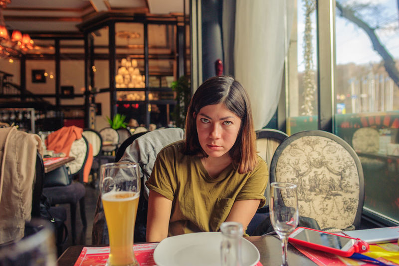 A pretty brunette girl is sitting at a table in a restaurant, in front of her is a glass of beer