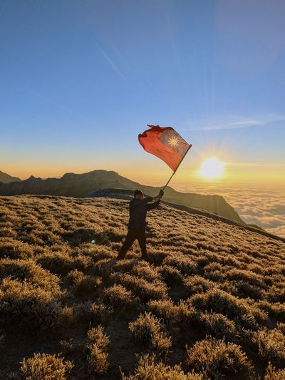 A man waving taiwan flag over the mountain in the sunrise