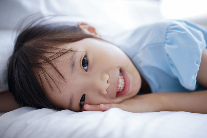 Close-up portrait of smiling girl lying on bed at home