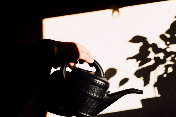 Cropped hand of man holding watering can against wall