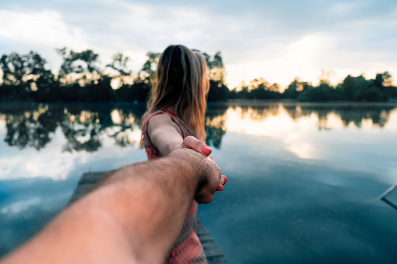 View of a woman from behind walking and watching the water of the lake at sunset holding a male hand