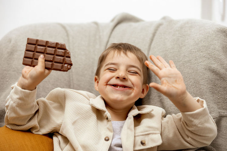 Little adorable boy sitting on the couch at home and eating chocolate bar. child and sweets